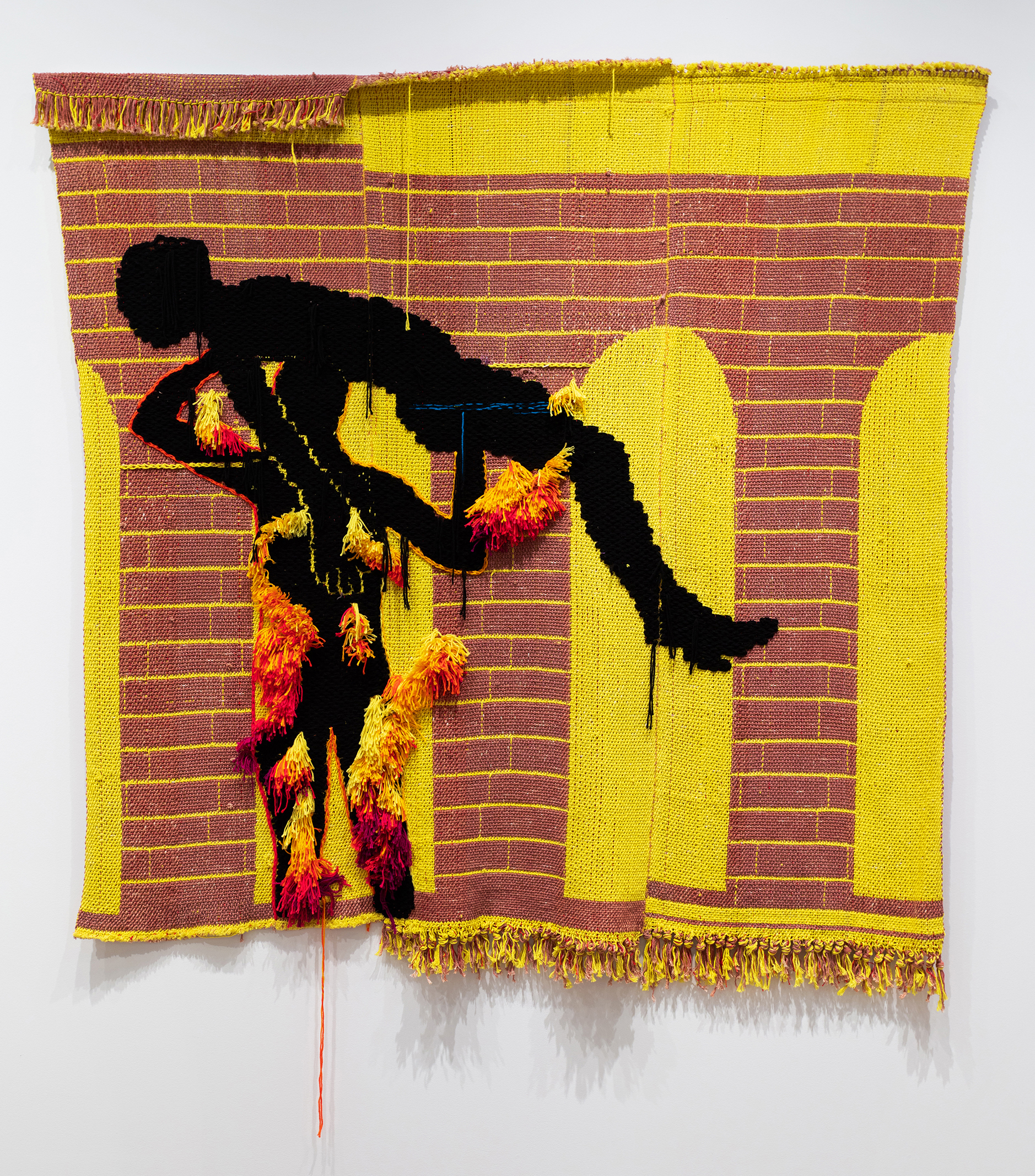 Weaving with an abstract figure holding up another with a brickwork patterned background.